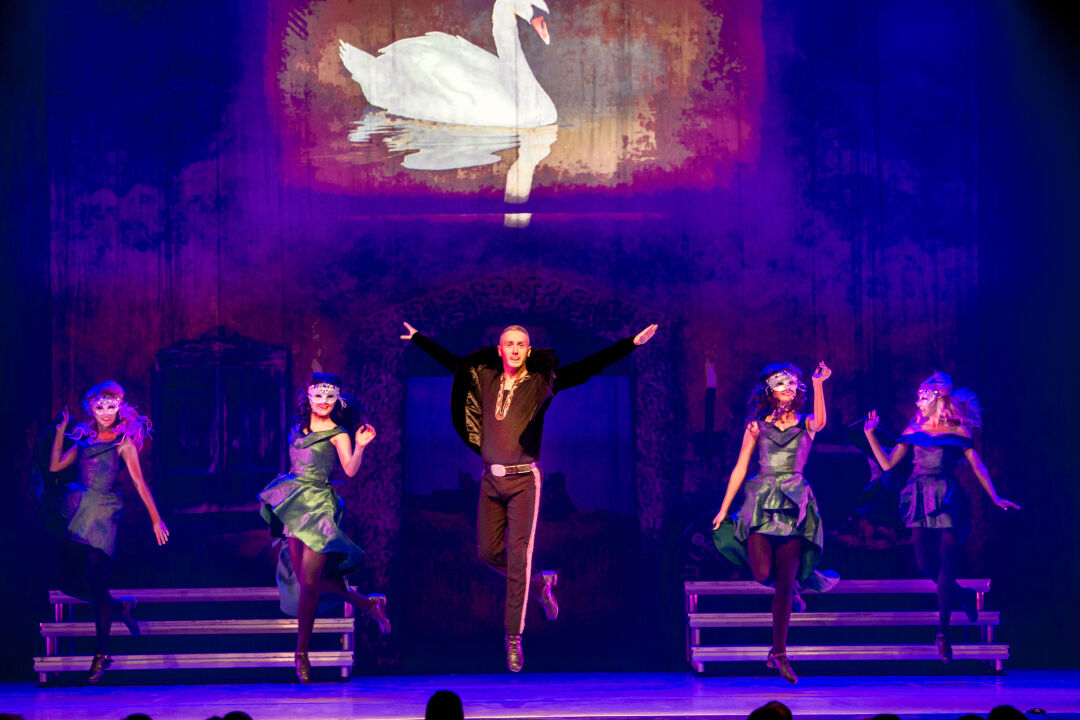 several dancers are lined up on stage. Male dancer stands in the middle, mid jump. Two female dancers stand either side of him.