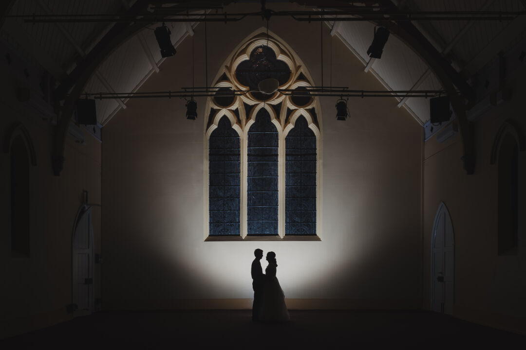 Wedding couple silhouetted against the stained glass window in the Church Theatre