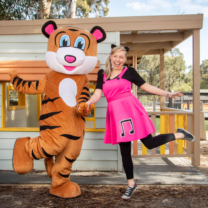 Sarah and Pevan the Tiger Mascot pose while holding hands and kicking one leg up with smiling faces